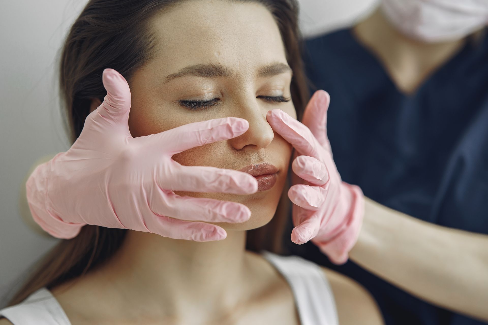 DermAesthetics practitioner consultation for facial harmonisation and skin rejuvenation DermAesthetics practitioner in pink clinical gloves examining a patient's face during an aesthetic skin clinic consultation